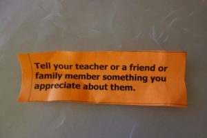 A crumpled orange‑colored “kindness fortune” slip pulled from a bucket, its edges folded from previous handling.